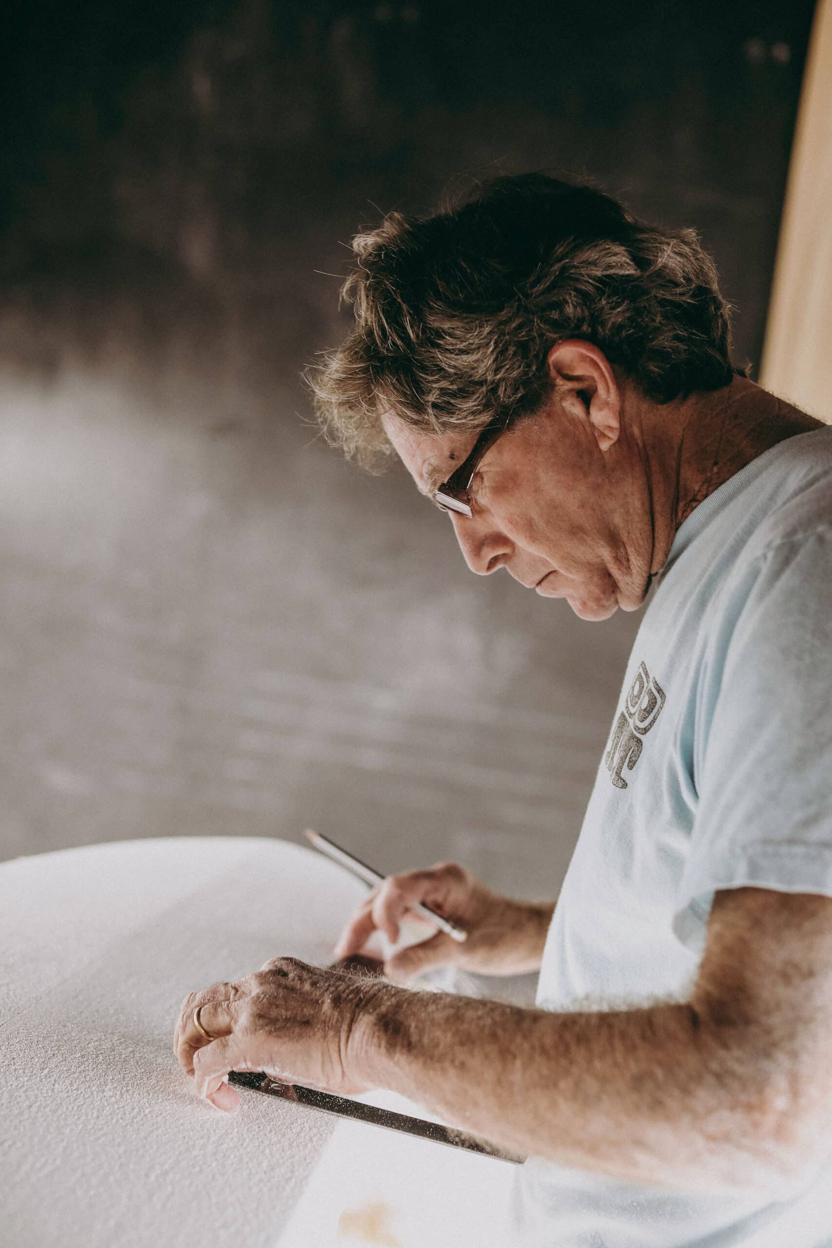 Shapers-Club- A man paints a surfboard on a table. -surfshop-surfboard