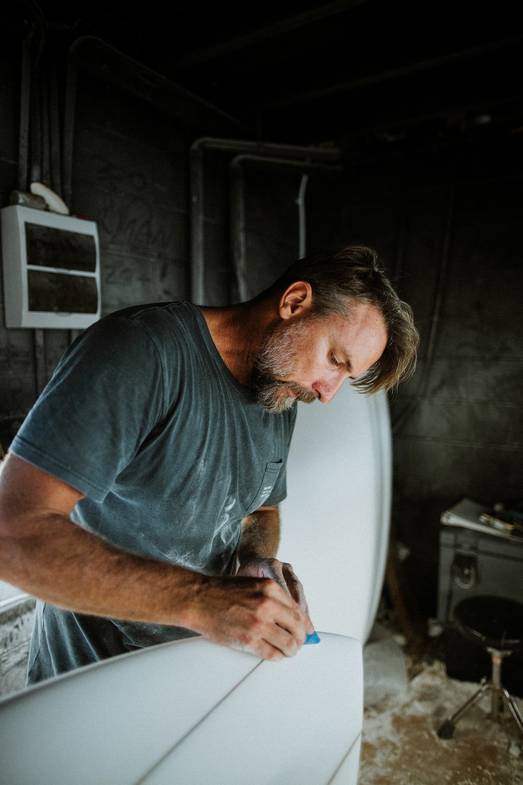 Shapers-Club- A man working on a surfboard in a garage. -surfshop-surfboard