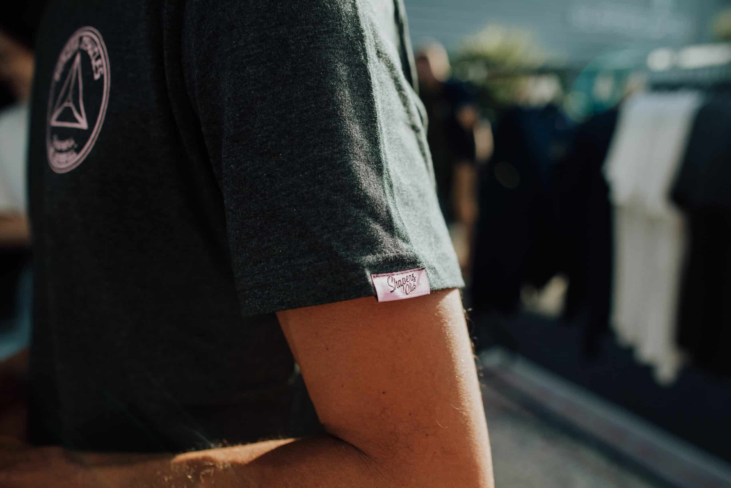 Shapers-Club- A man wearing a gray t-shirt with a logo on it. -surfshop-surfboard