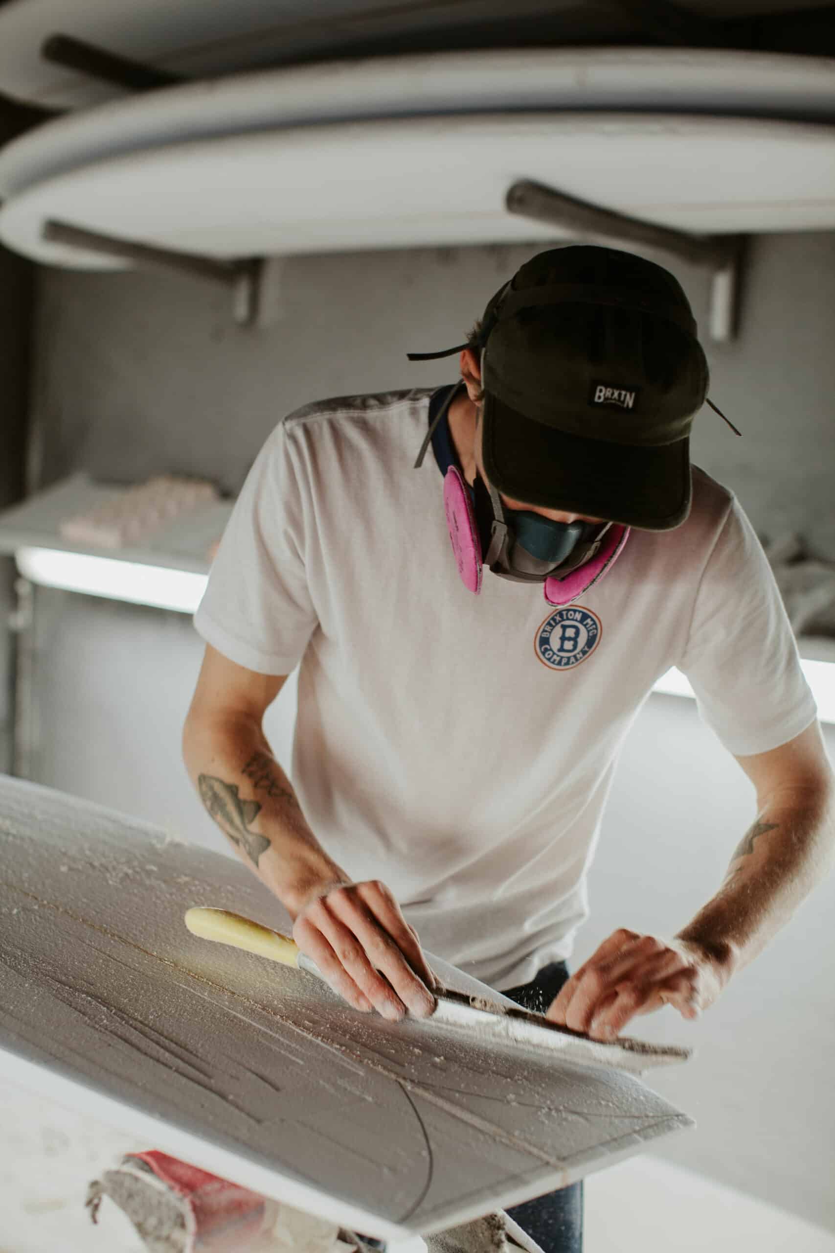 Shapers-Club- A man works on a surfboard in a workshop. -surfshop-surfboard