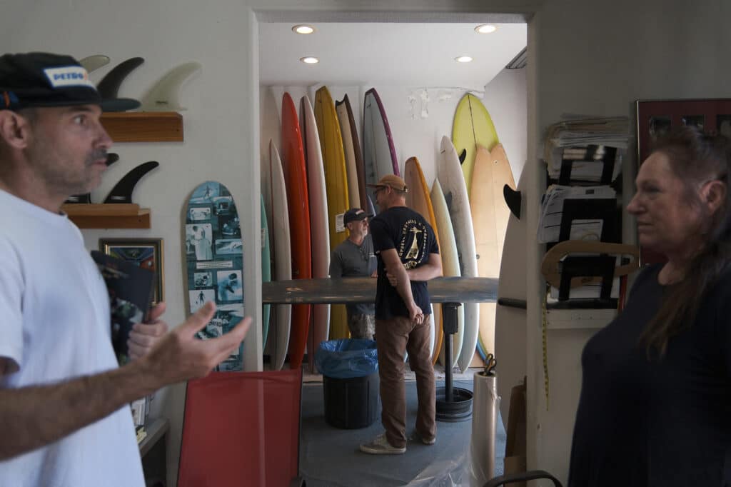 Shapers-Club- Des gens conversant dans un atelier de surf entourés de planches de surf colorées. -surfshop-surfboard