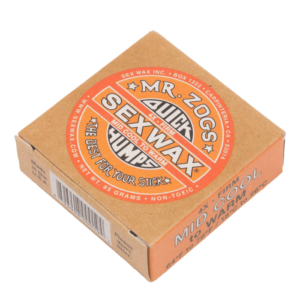 Shapers-Club- A rectangular can of Sexwax - Mid Warm surf wax is presented. The orange packaging features circular branding in red, white and black. The text indicates "Quick Humps", "Mid Warm to Cool" and "Firm". The 85-gram weight and non-toxic properties are indicated. -surfshop-surfboard