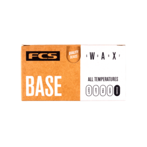 Shapers-Club- Une boîte en carton de FCS - Wax - Base sur fond vert. L'étiquette indique « FCS BASE », ce qui indique qu'elle convient à « toutes les températures ». En mettant l'accent sur les « perles de qualité », la cire classe les températures comme fraîches, chaudes, tropicales et froides. -surfshop-surfboard