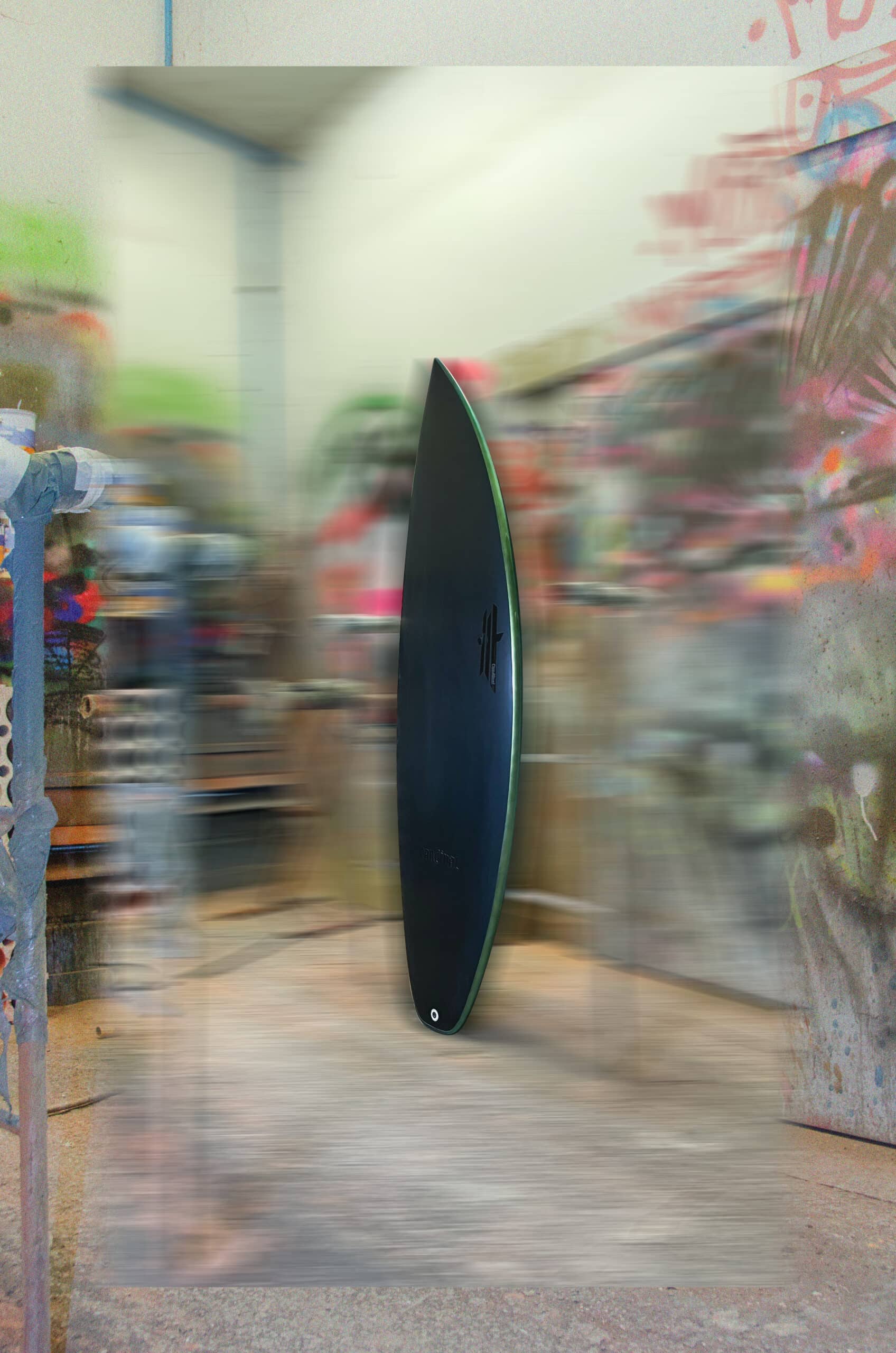 Shapers-Club- Une planche de surf élégante et sombre Fire Arrow 6'0" x 20" avec un logo blanc subtil se dresse verticalement dans un atelier au milieu d'un arrière-plan flou d'œuvres d'art et d'outils colorés peints à la bombe, créant une ambiance artistique. -surfshop-surfboard