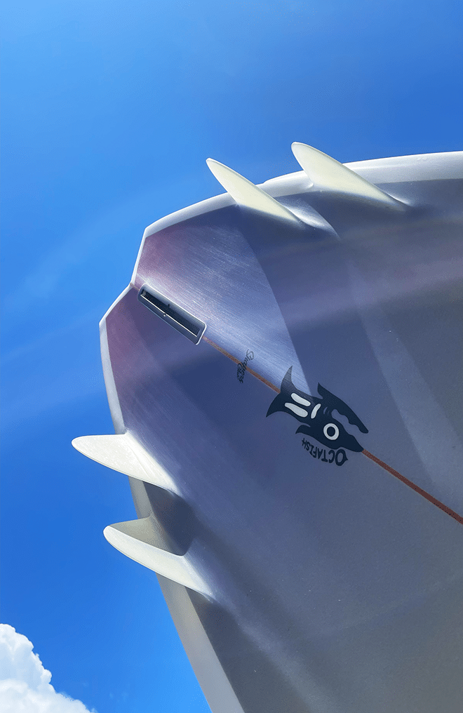 Shapers-Club- Una tavola da surf Octafish di un metro e ottanta, caratterizzata da un'elegante superficie bianca con pinne multiple, è fotografata dal basso in un cielo blu brillante. Ha una grafica nera di grande effetto e reca il logo '02" e il nome "Octafish", mentre scivola sotto soffici nuvole ai margini dell'immagine. -surfshop-surfboard