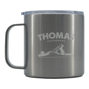 Shapers-Club- The beige Shapersclub Thomas Surfboards isothermal mug features a transparent lid and handle with an engraved logo of a person surfing a wave, along with the text "THOMAS SURFBOARDS". -surfshop-surfboard