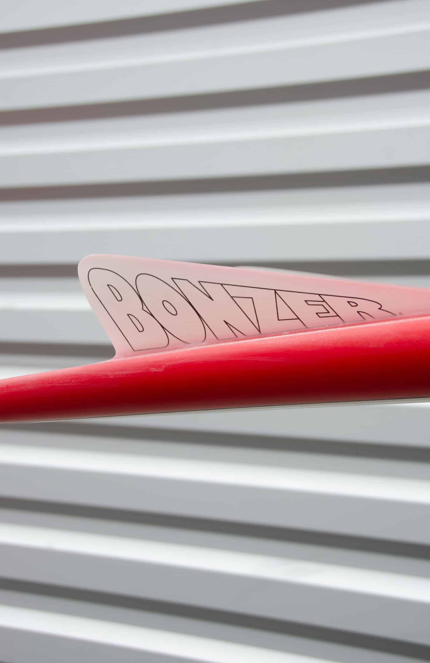 Shapers-Club- Gros plan d'une dérive de planche de surf rouge Russ Short 6'2" x 19' 1/2" x 2' 1/2" étiquetée "BONZER", posée sur un revêtement horizontal blanc. -surfshop-surfboard
